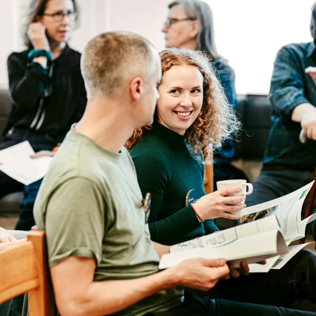 Bilden visar en grupp människor som verkar befinna sig i ett mötesrum eller en föreläsningssal. I ...